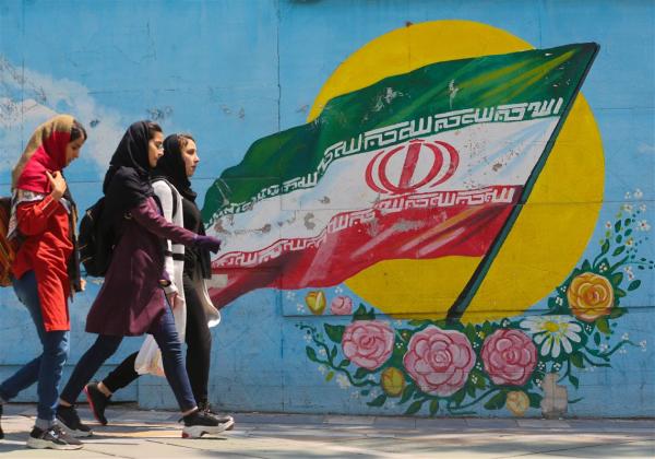 Young girls walk in front of a mural of the Iranian national flag in Tehran. ATTA KENARE / AFP/Getty Images